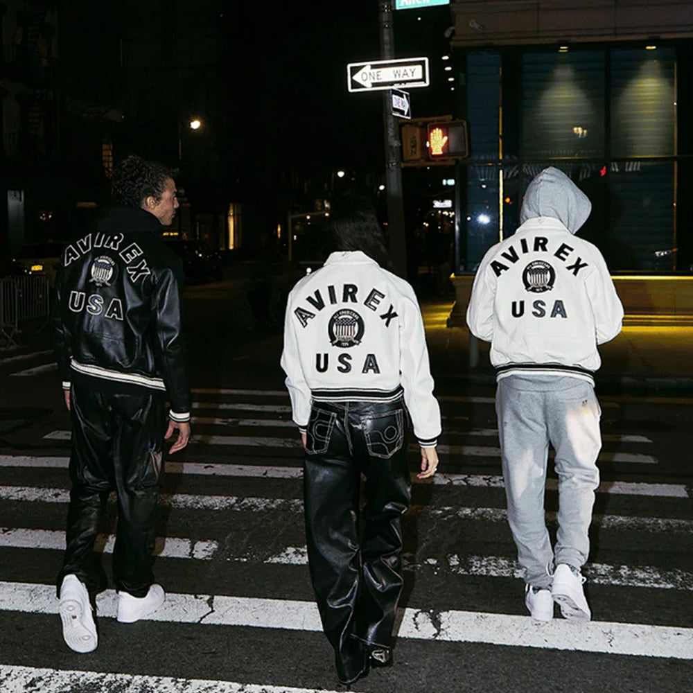 Three people wearing Avirex USA jackets crossing a street at night.