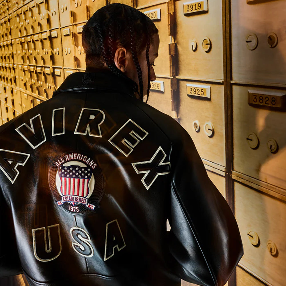 Person wearing a black leather jacket with 'AVIREX USA' branding in front of gold safe deposit boxes.