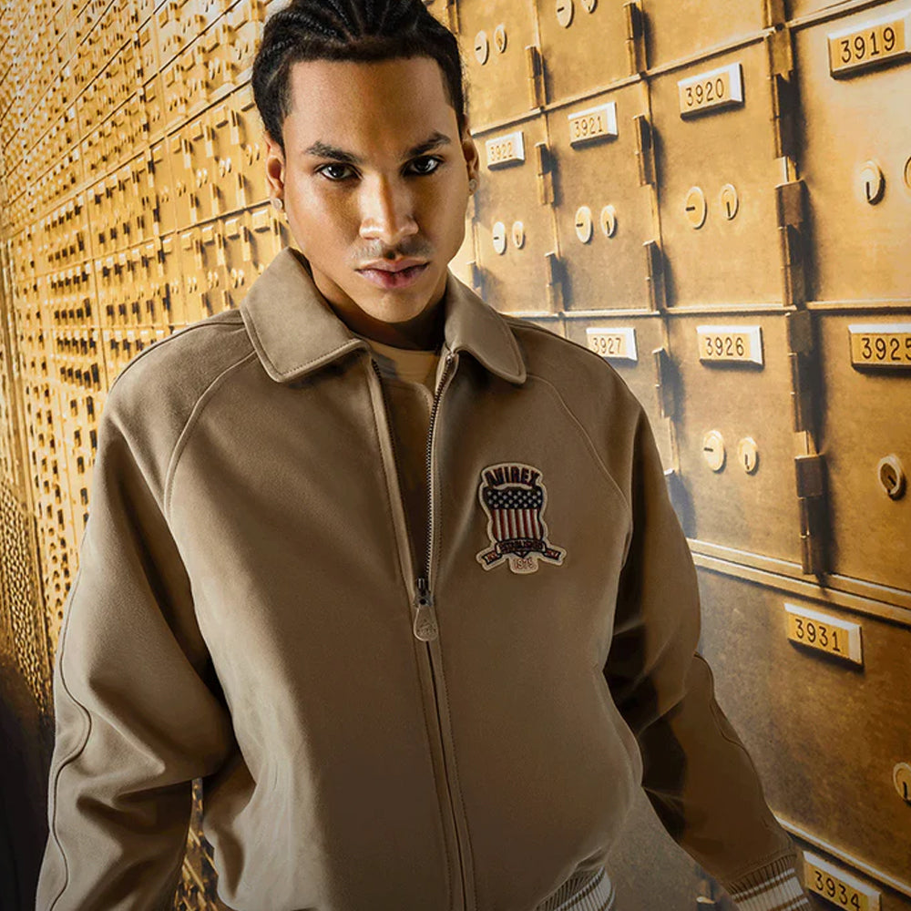 Man wearing a beige jacket with a logo in front of a row of gold safe deposit boxes.