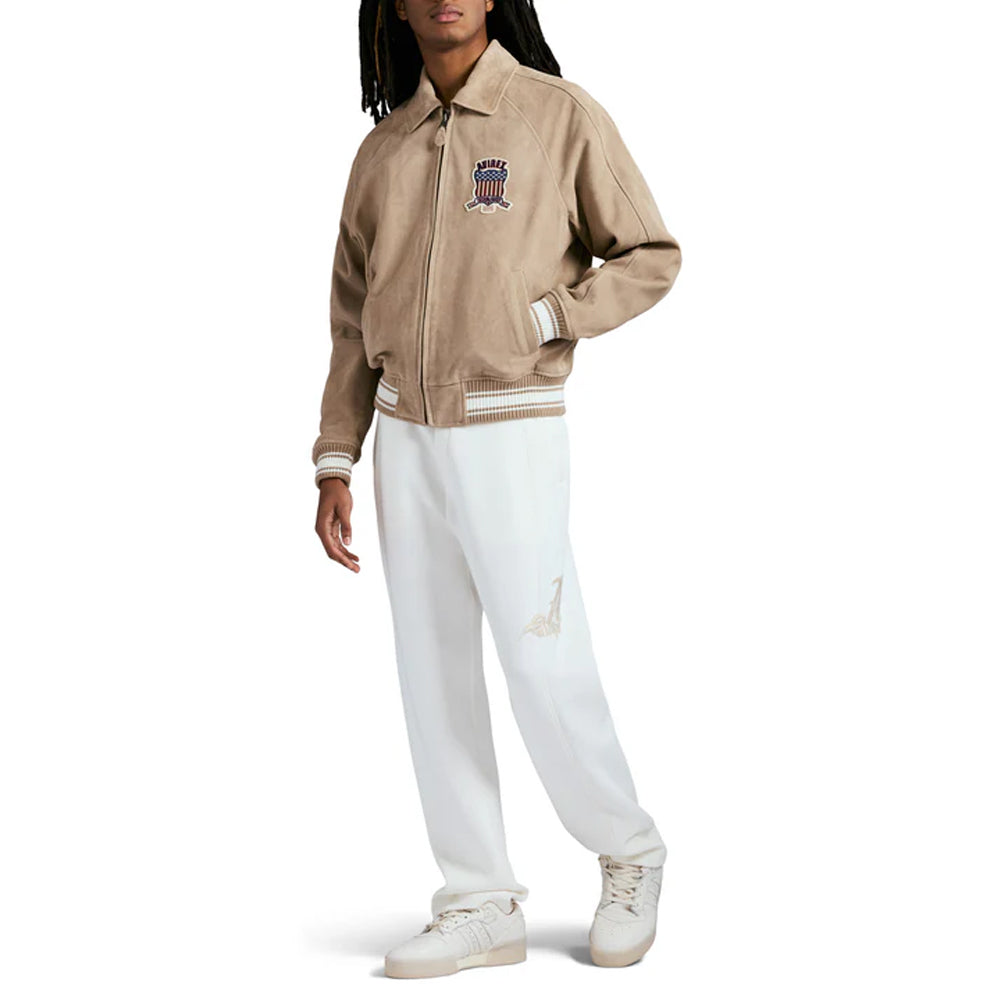 Person wearing a beige jacket with a logo and white pants on a white background