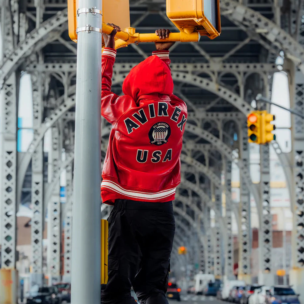 Person wearing a red Avirex USA jacket on a bridge with traffic lights.