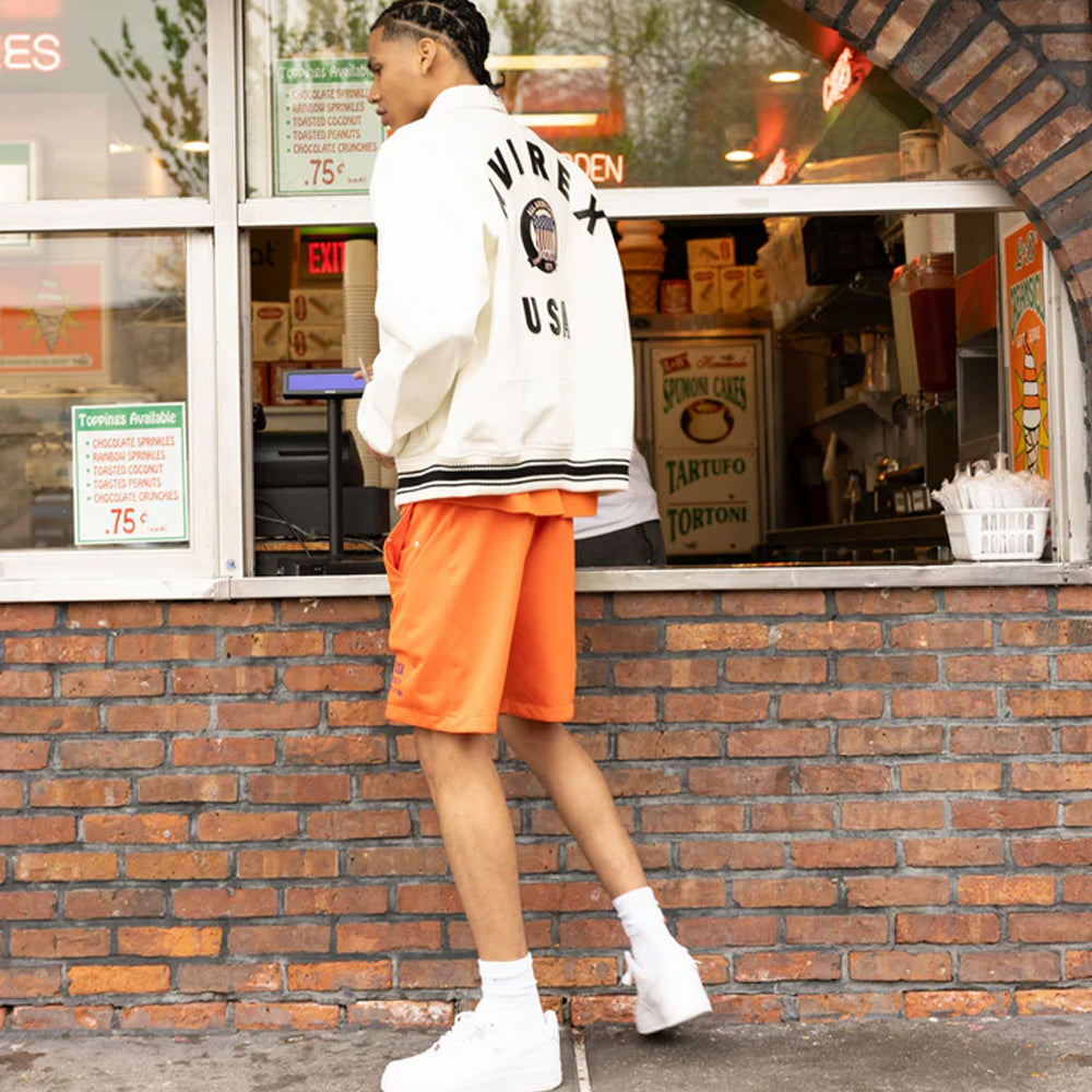 Person wearing a white jacket with 'Virex USA' branding and orange shorts standing in front of a brick building.