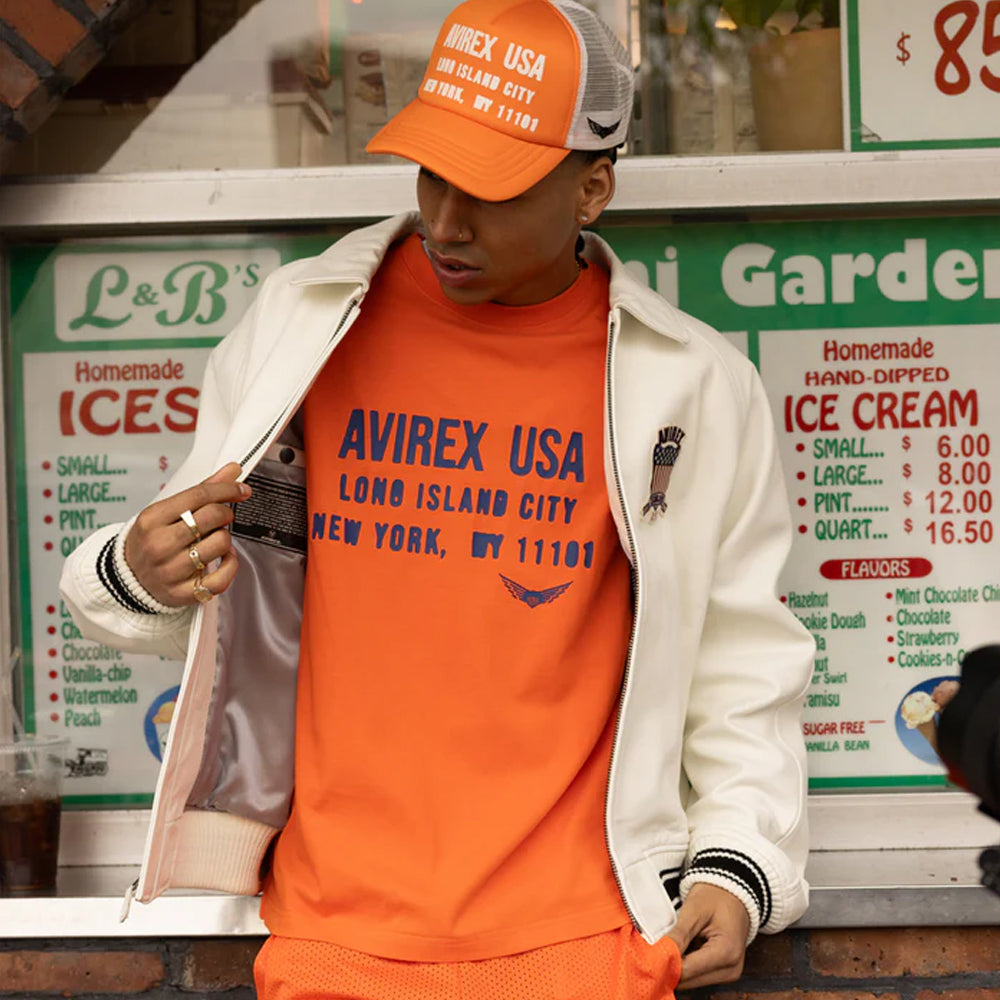 Person wearing an orange Avirex USA sweatshirt and cap in front of a ice cream shop.