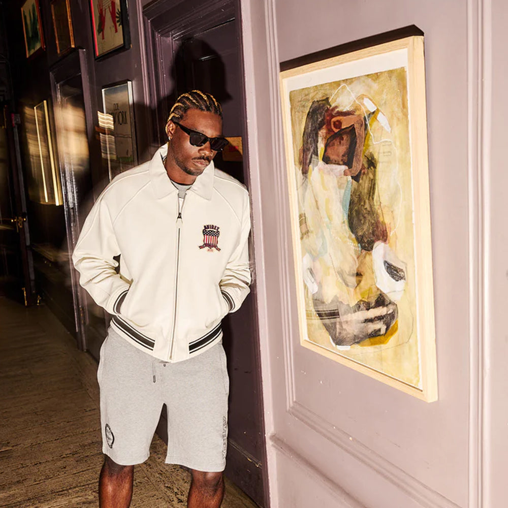 Man in a white tracksuit standing next to a painting of a woman with a bird on a wall.