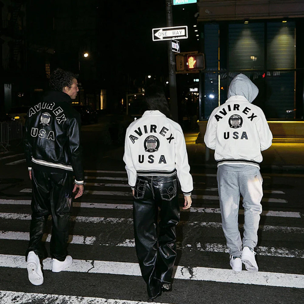 Three people wearing Avirex USA jackets on a city street at night.