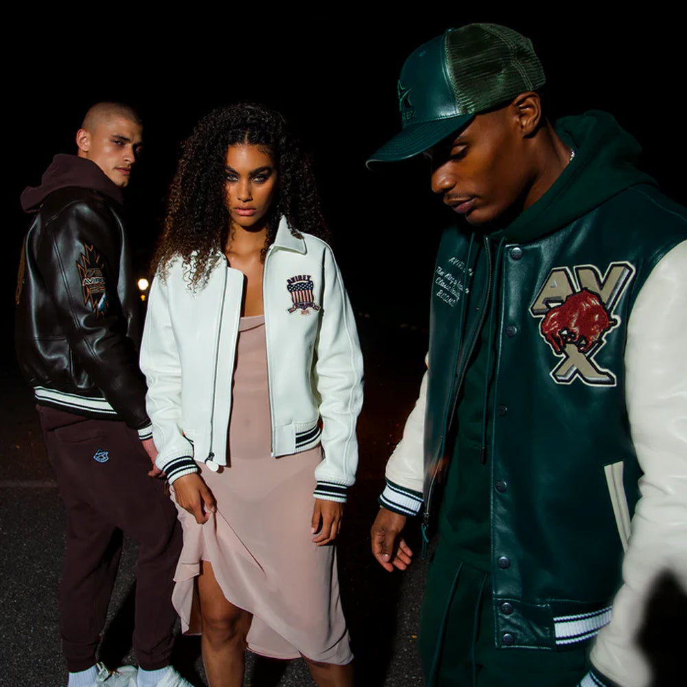 Three people wearing varsity jackets standing together at night.