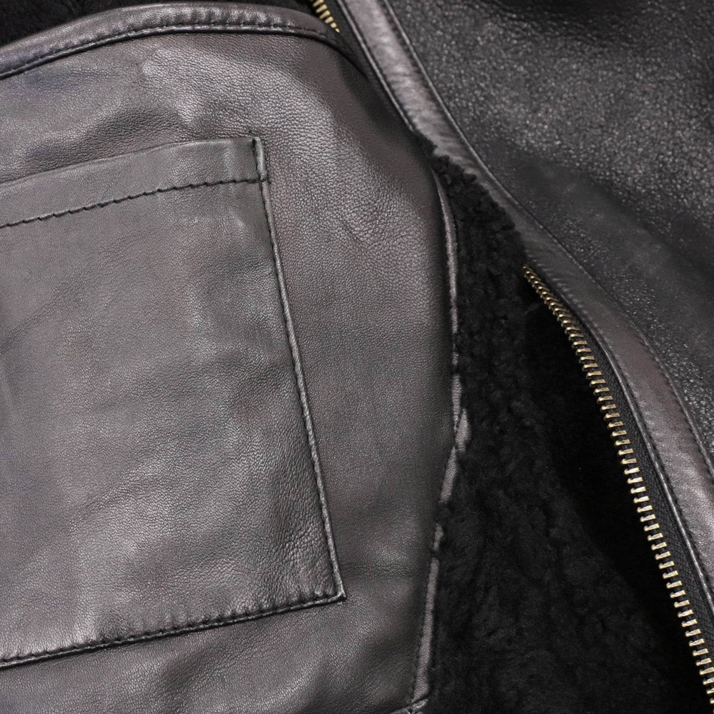 Close-up of leather top-entry interior patch pocket beside full black shearling lining and antique-brass zipper