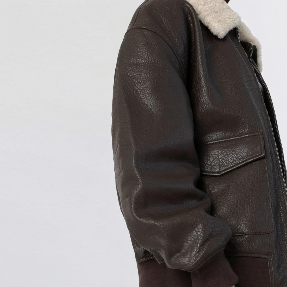 Close-up of pebbled brown cow leather, rib-knit cuff and front flap pocket on oversized bomber jacket