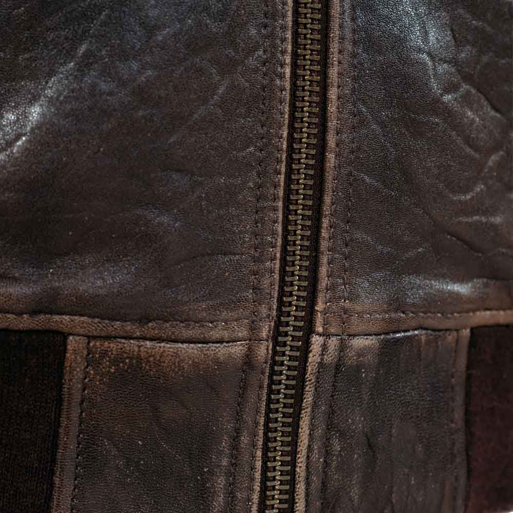 Macro view of waist zipper, tonal topstitching and rib-knit hem on men’s vintage brown flight jacket