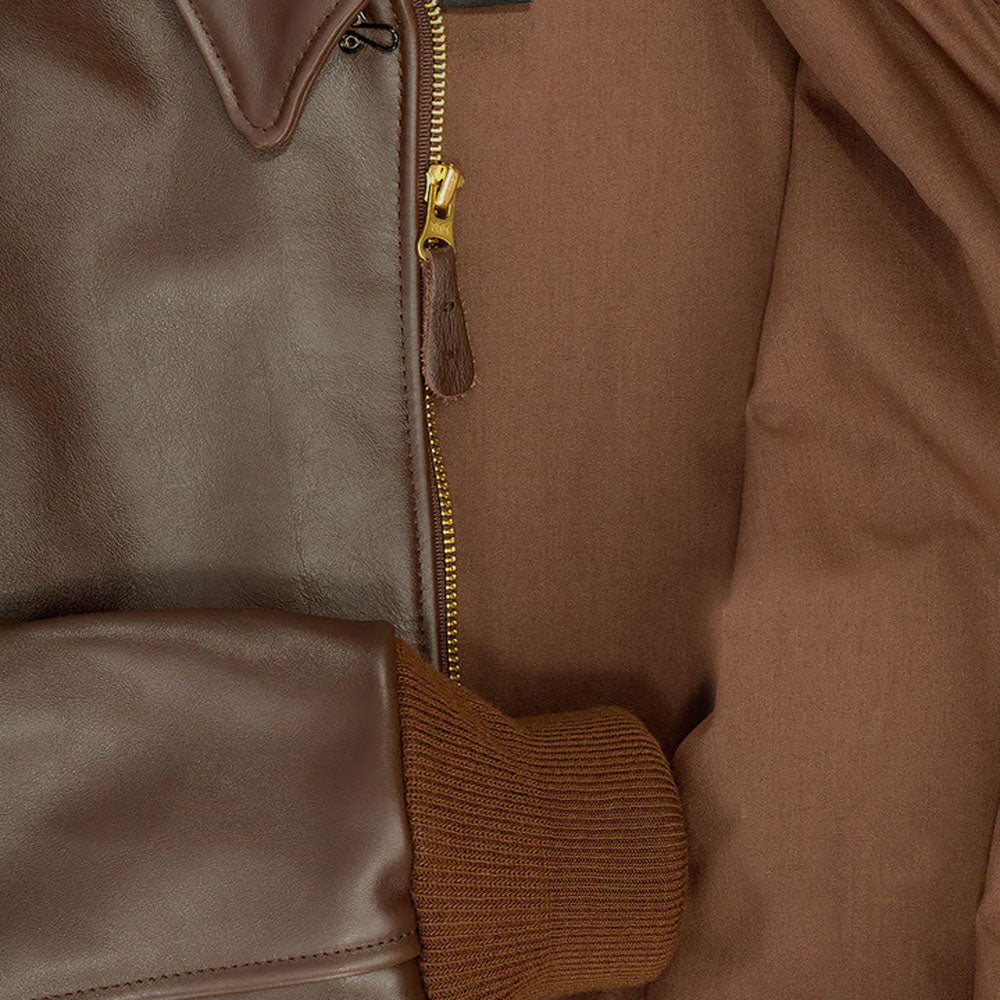 Macro detail of heavy-duty brass zipper, leather puller, throat hook, and russet cotton lining on A-2 horsehide jacket.