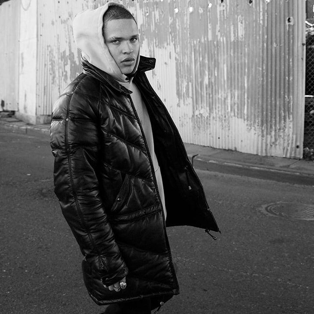 Man wearing black leather V-parka coat open over hoodie in urban street style shoot