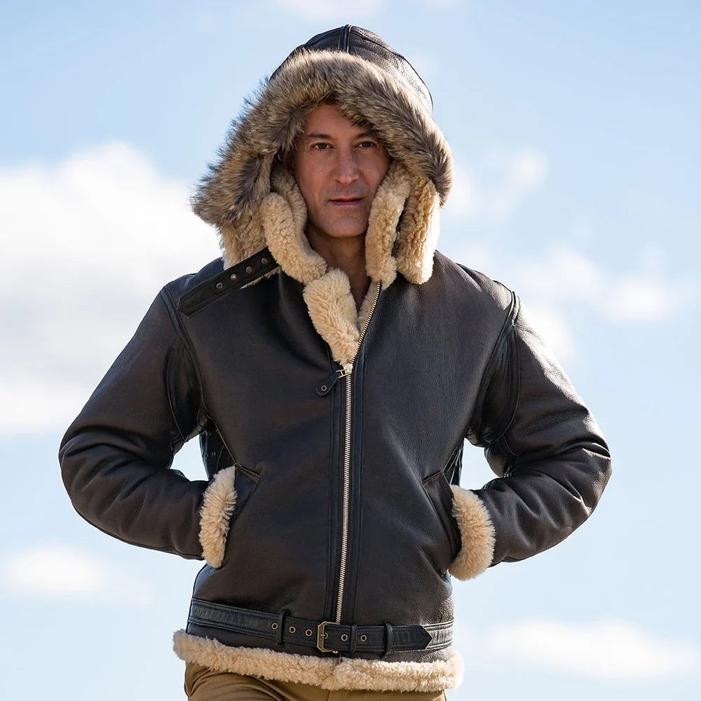 Model wearing men's hooded B-3 dark brown shearling aviator jacket with natural raccoon fur trim outdoors.