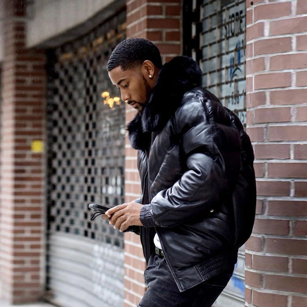 Side profile view of a man on the street wearing the heavy black insulated leather bomber jacket, checking his smartphone.