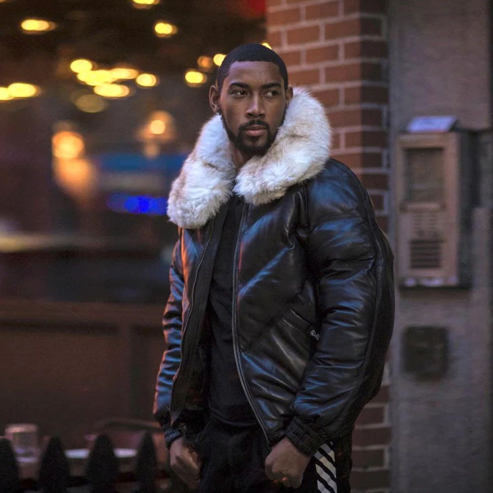 A model standing outside looking forward wearing the black sheepskin leather down puffer coat with a plush off-white fox fur collar.
