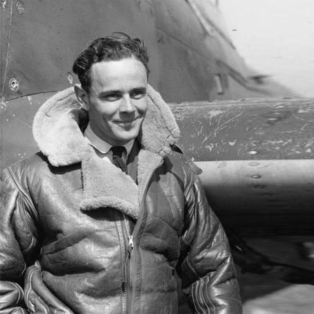 Black and white image of a man wearing a shearling leather jacket, smiling while standing with the front zipper of his jacket closed, showcasing the classic style and warmth of shearling jackets.