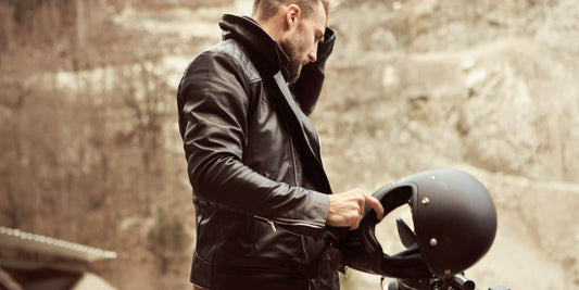 A rider wearing a vintage-wash sheepskin leather jacket sitting on a modern cafe racer motorcycle.
