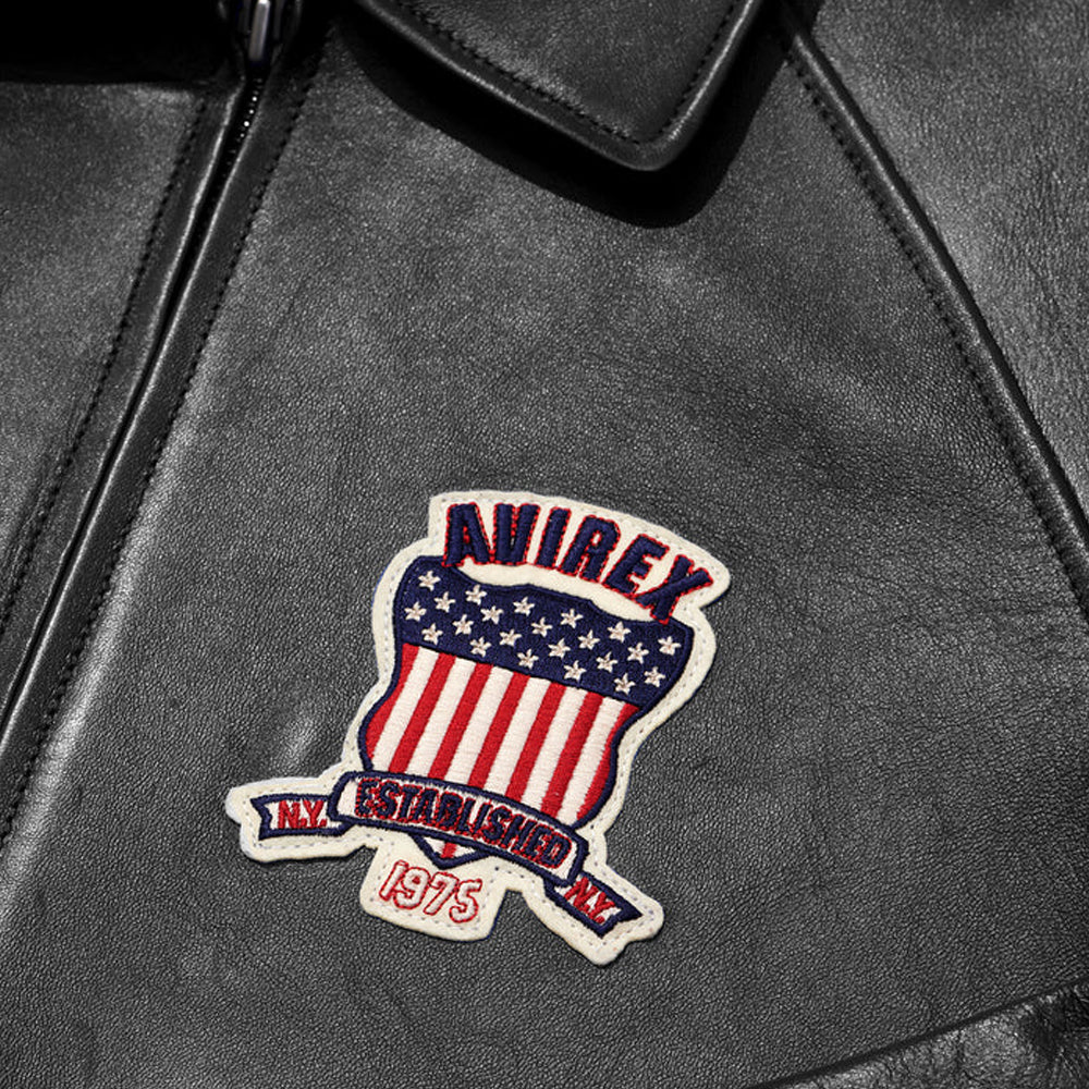 Close-up of a black leather jacket with an embroidered patch featuring an American flag design and text.