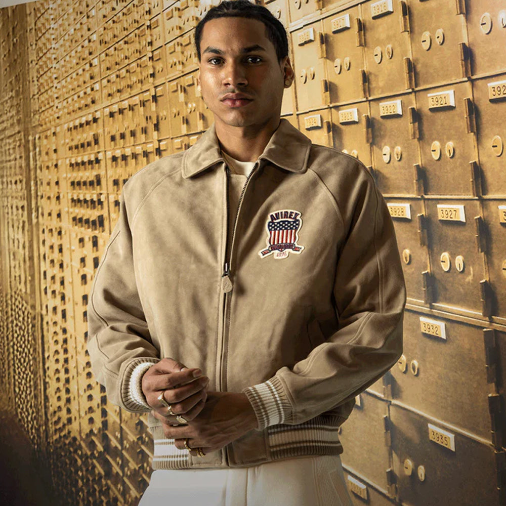 Man wearing a beige jacket with a logo in front of gold safe deposit boxes.