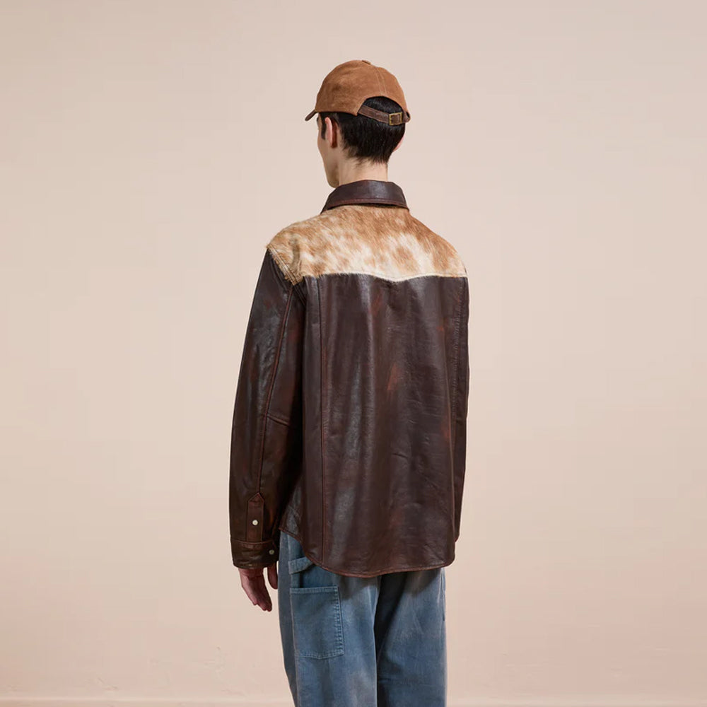 Person wearing a brown leather jacket with a cowhide pattern on a beige background