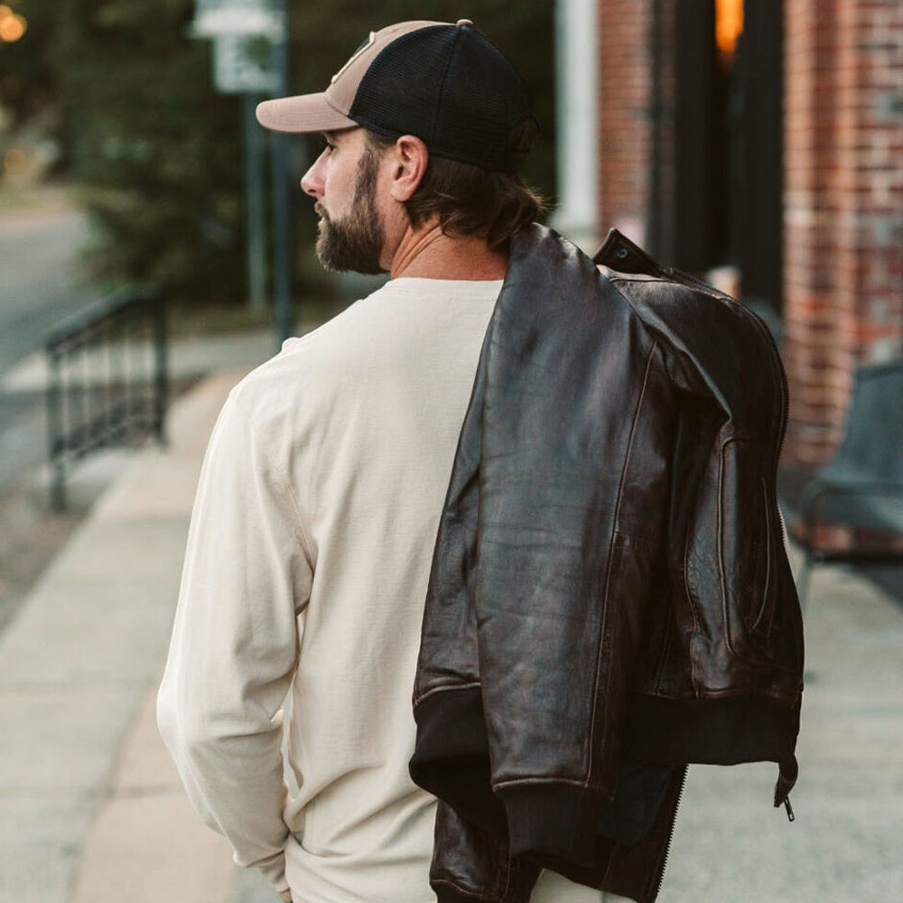 Man wearing Men’s Vintage A2 Bomber Leather Jacket over his shoulder, showcasing the back view and classic aviator design.