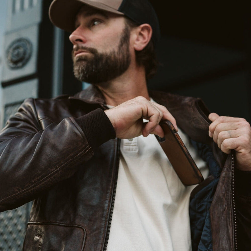 Close-up of model wearing Men’s Vintage A2 Bomber Leather Jacket, placing a mobile phone in the inner pocket, highlighting its functionality.