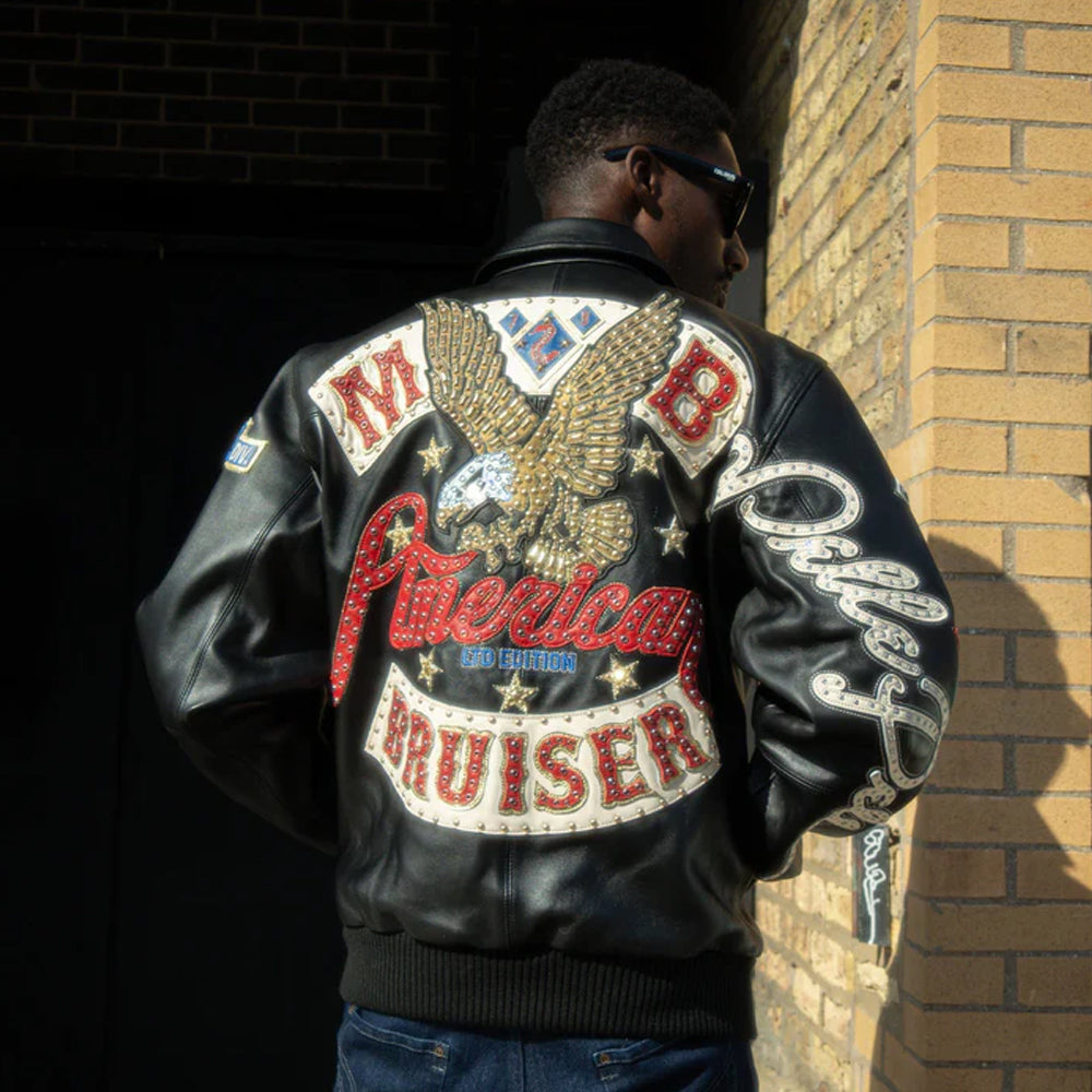 Person wearing a Pelle Pelle black leather jacket with an eagle emblem and text, standing against a brick wall.