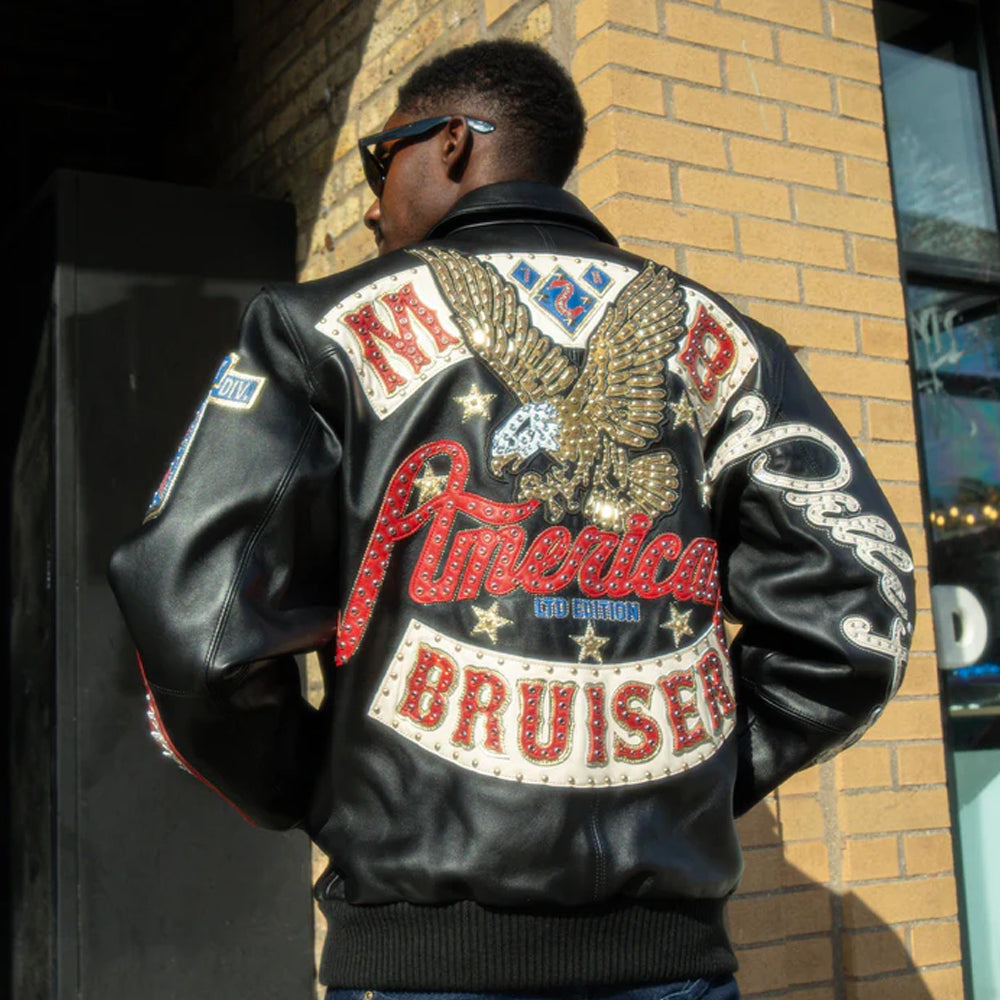 Person wearing a Pelle Pelle black leather jacket with colorful text and an eagle design, standing against a brick wall.
