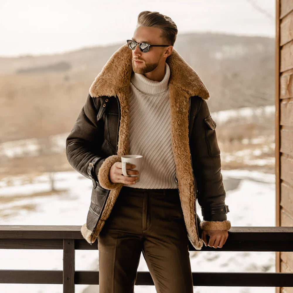 Man wearing B3 Aviator Sheepskin Jacket with open front zipper, holding a tea cup, and looking to the side, showcasing the jacket's stylish design.