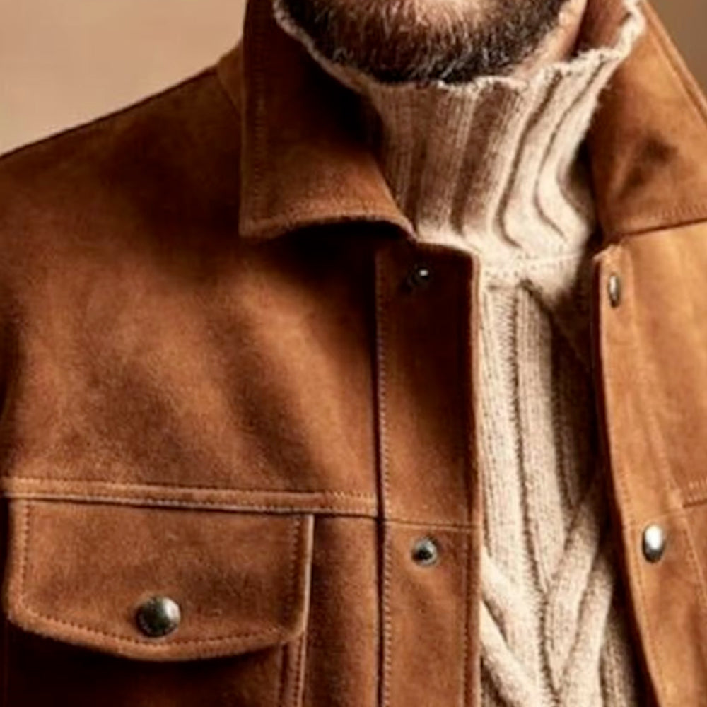 Close-up of the chest pocket of a brown suede leather jacket, showcasing fine stitching and button detail.