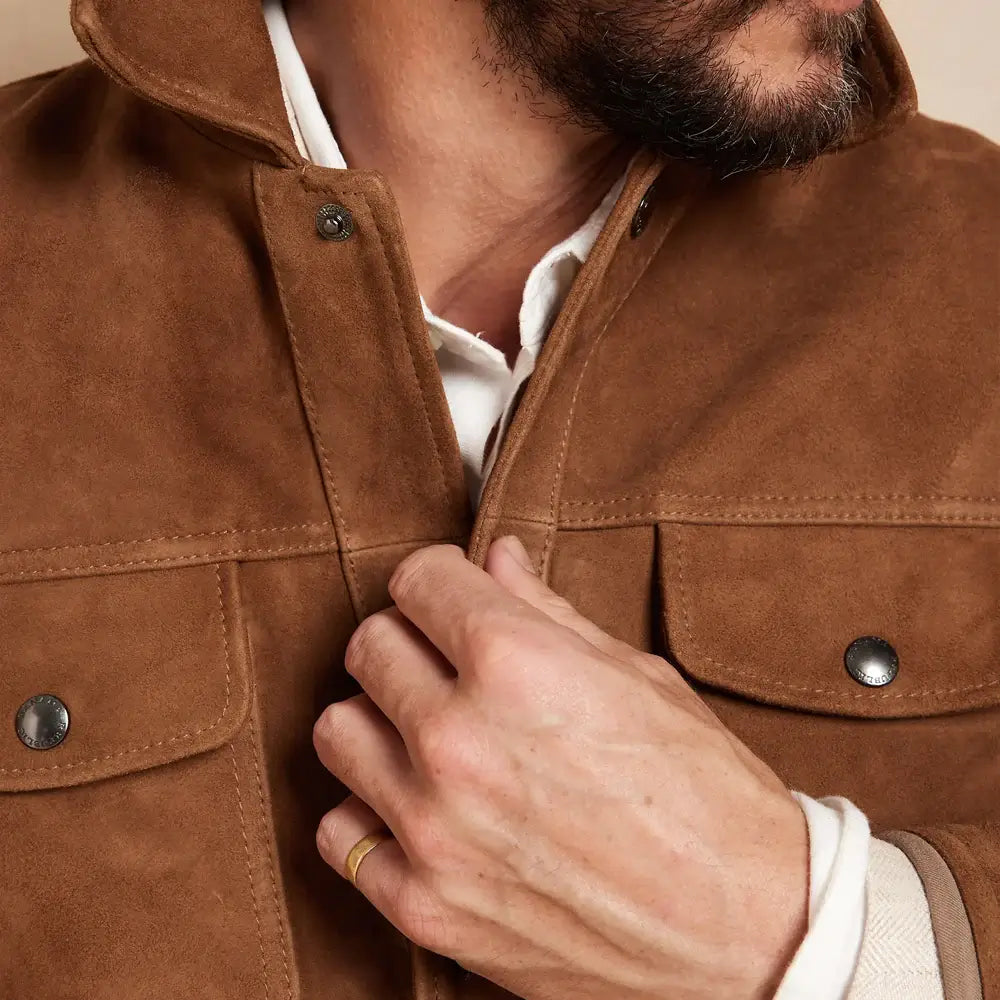 Close-up view of two front pockets on the brown suede leather jacket, with a hand adjusting the front button.