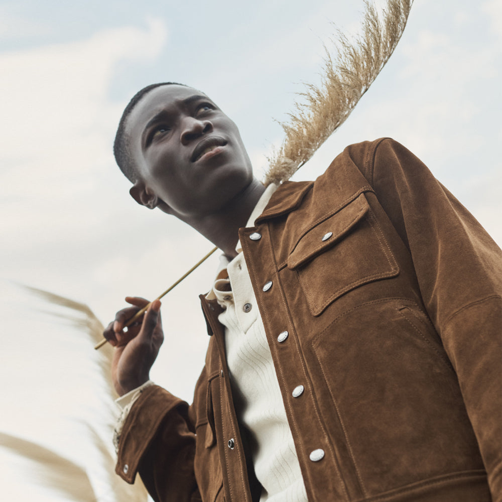 Man wearing a brown suede leather jacket, captured from a low-angle side view, showcasing details and fit.