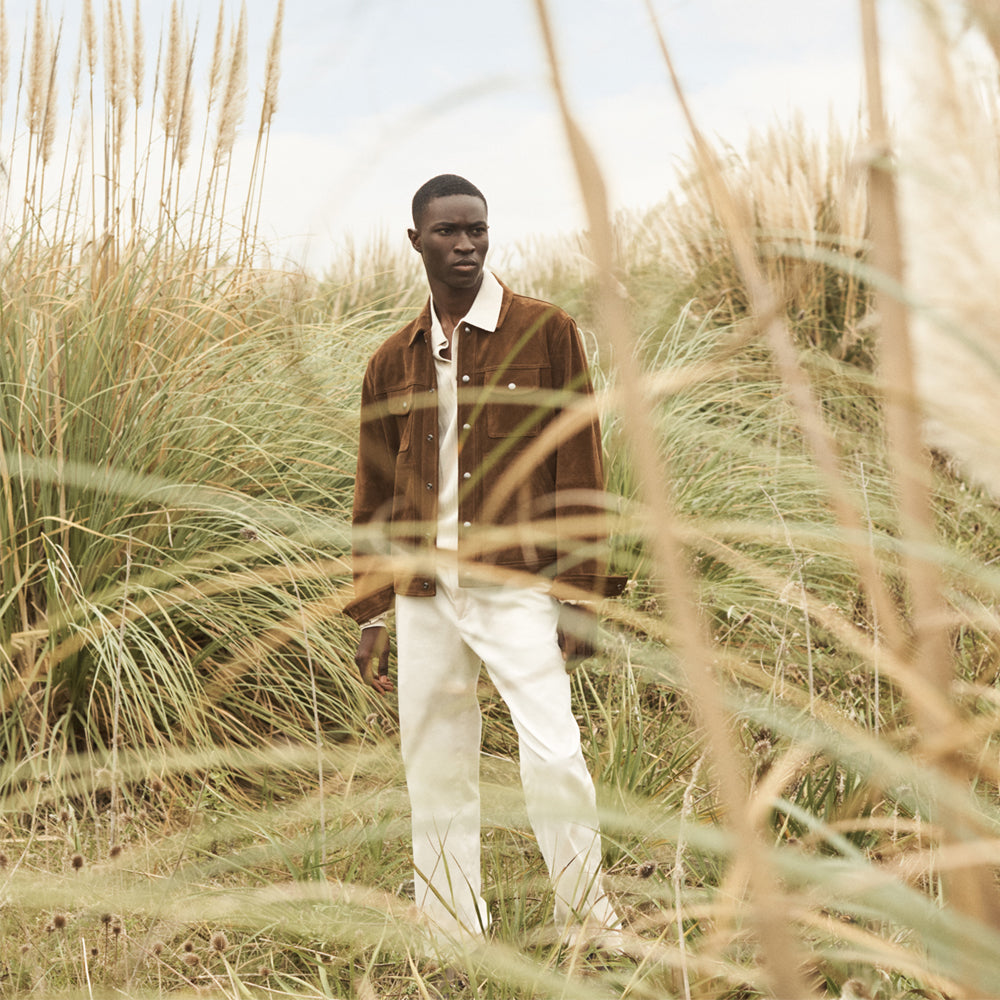 Man in a brown suede leather jacket standing outdoors, showcasing the jacket in natural light.