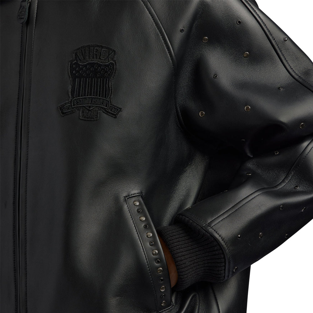 Detail of tonal Avirex chest crest, studded pocket border, rib-knit cuff and spaced sleeve hardware on black leather