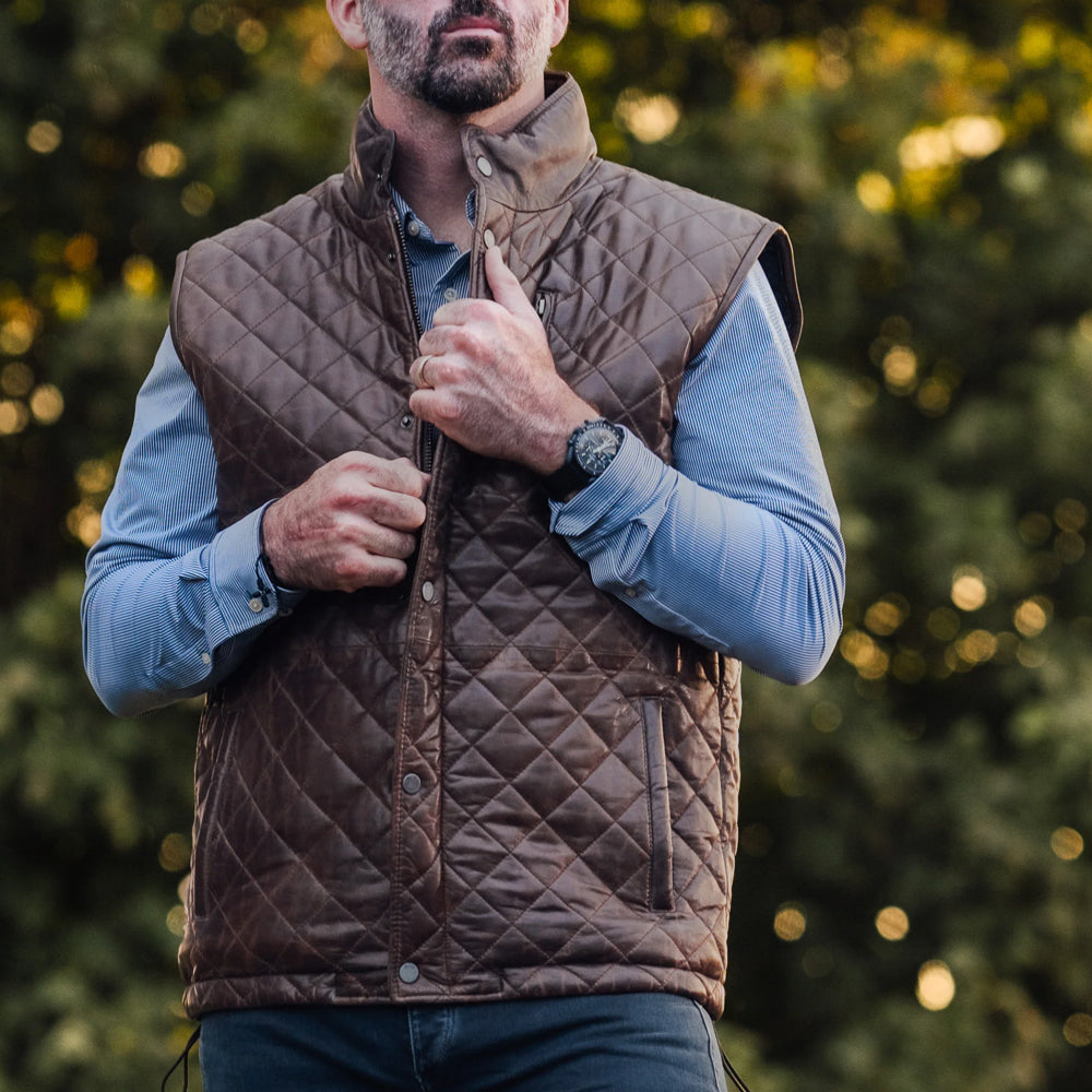 Lifestyle shot of a man wearing the dark brown biker leather vest with the front zipper halfway open.