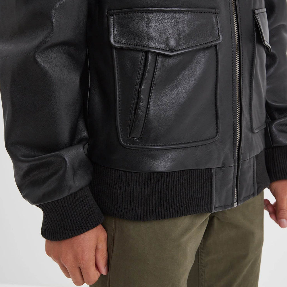 Detail of black dual-entry flap patch pocket with vertical hand opening, rib-knit cuff and bomber waistband.