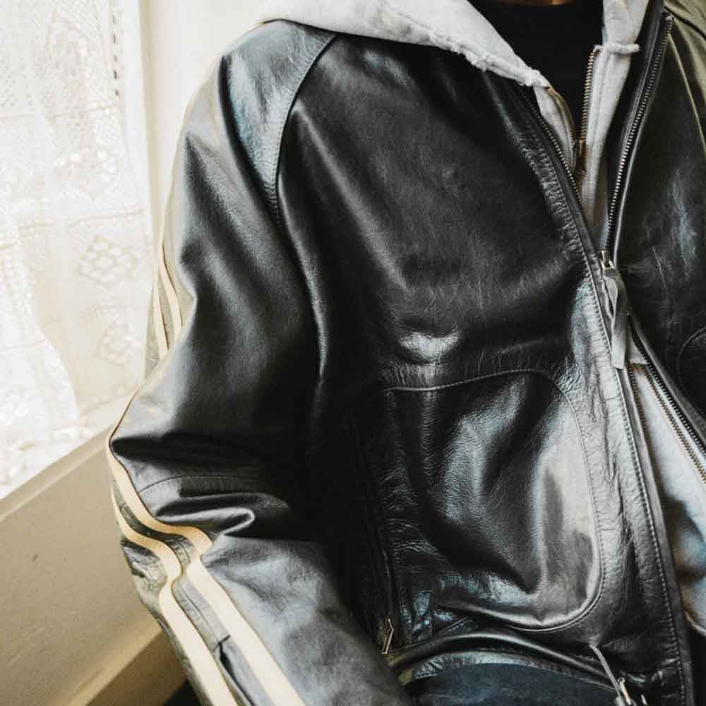 Close-up of smooth black cowhide, curved zip-pocket panel and cream sleeve bands on men’s vintage track jacket