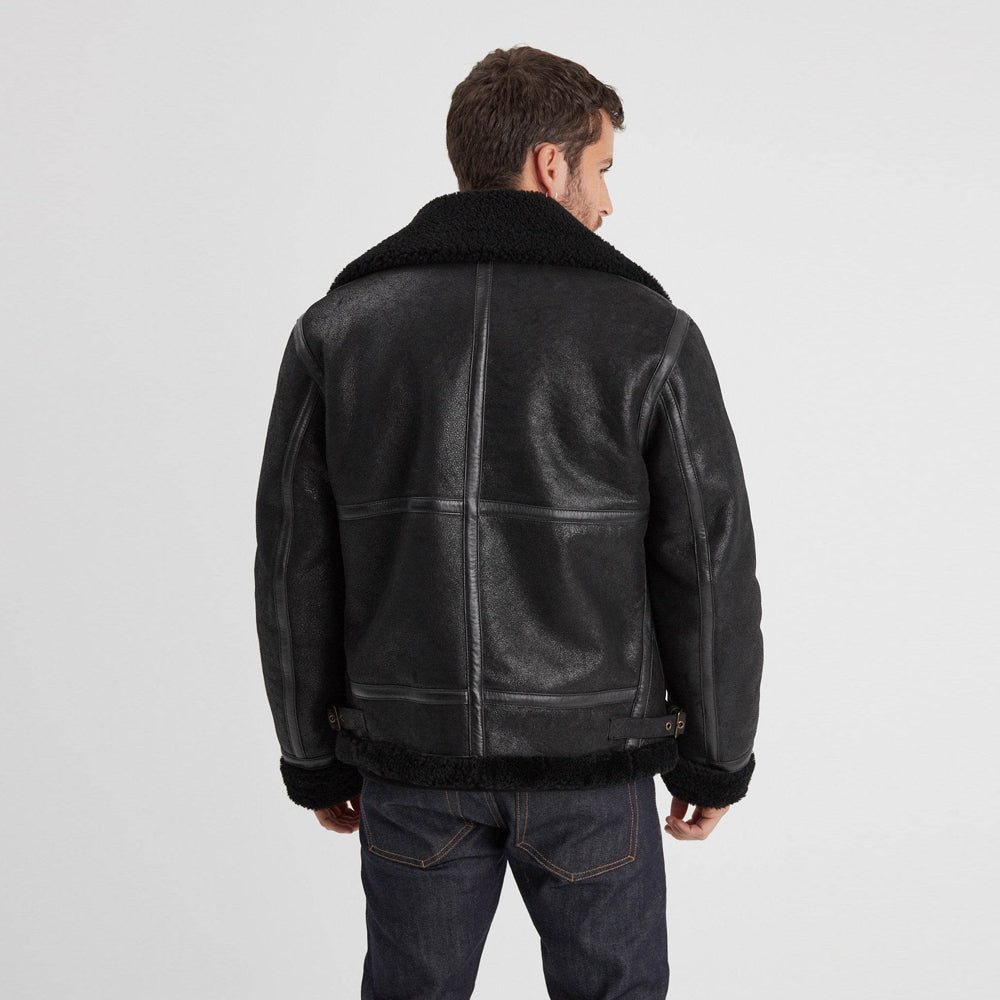 Rear view of black sheepskin flight jacket showing vertical center binding, horizontal panel seams, and waist adjusters