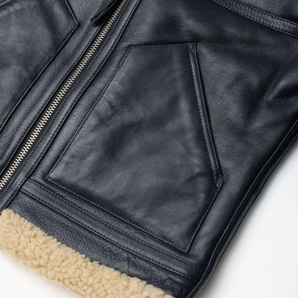 Close-up of diagonal hand-warmer slant pocket and exposed beige shearling hem on black sheepskin leather jacket