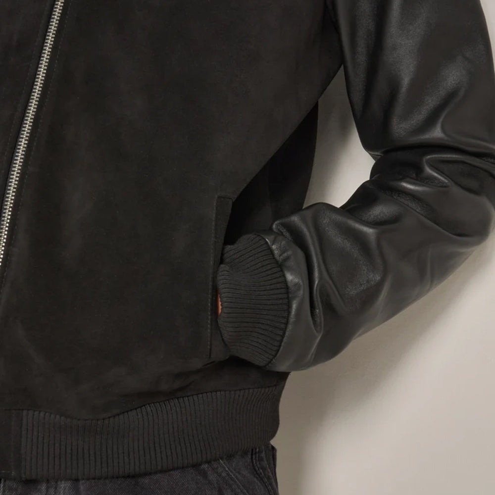 Close-up of black suede bomber jacket with open angled welt pocket, smooth leather sleeve and rib-knit cuff and waistband