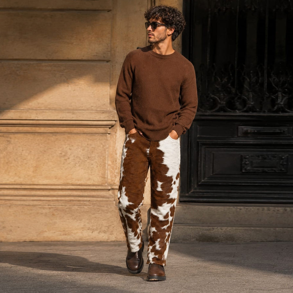 Men's Boho-chic fashion featuring cow print leather pants and a brown knit sweater.