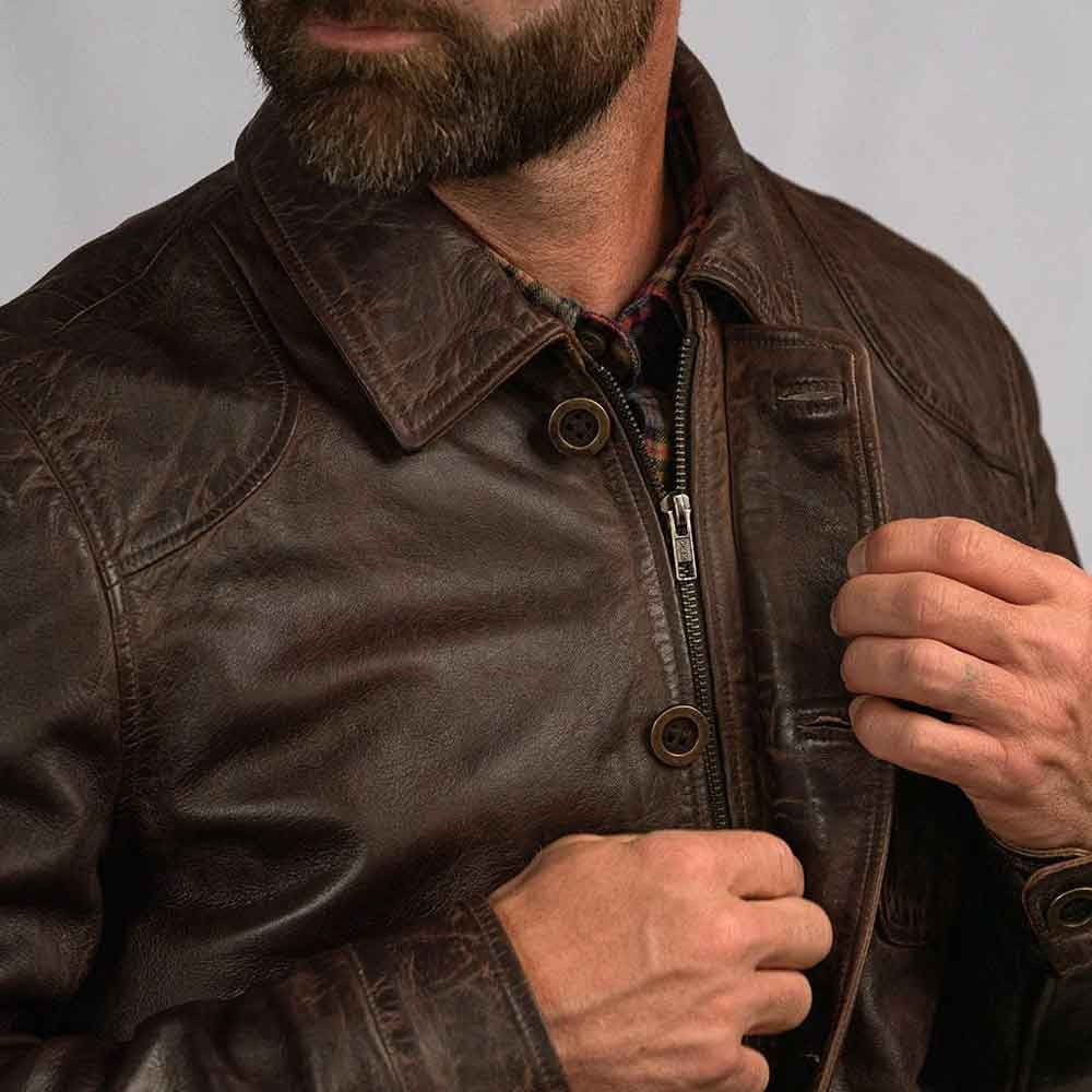 Close-up of dark brown leather field jacket showing antique-brass YKK zipper beneath the button-front placket