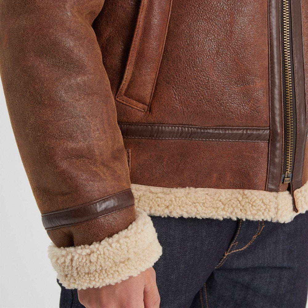 Close-up of brown sheepskin flight jacket showing cream shearling cuff, fleece-trimmed hem, dark binding, and antique zipper