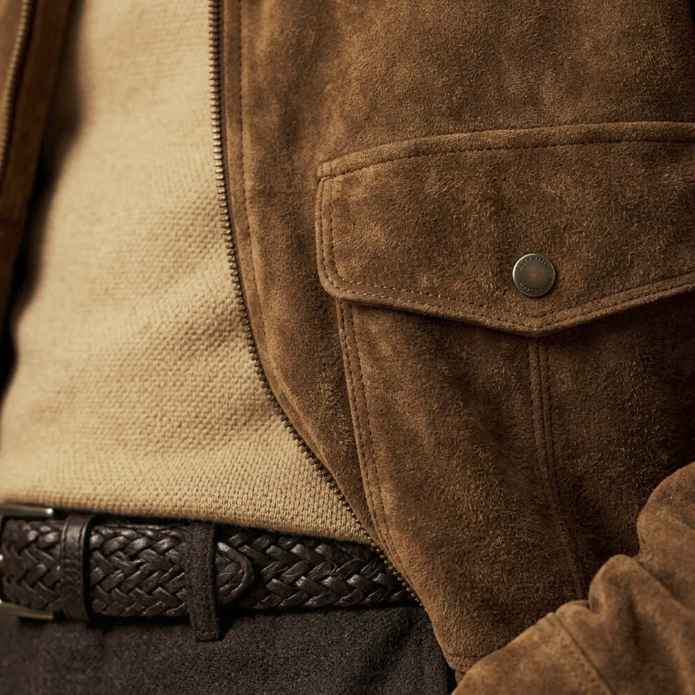 Close-up of brown suede chest patch pocket with angular flap, antique-tone snap, tonal topstitching and YKK zipper edge.