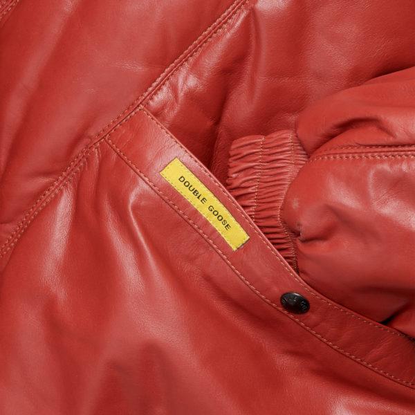 Close-up details of a welt-angled hand-warmer pocket with a branded metal snap-button closure on red calfskin.