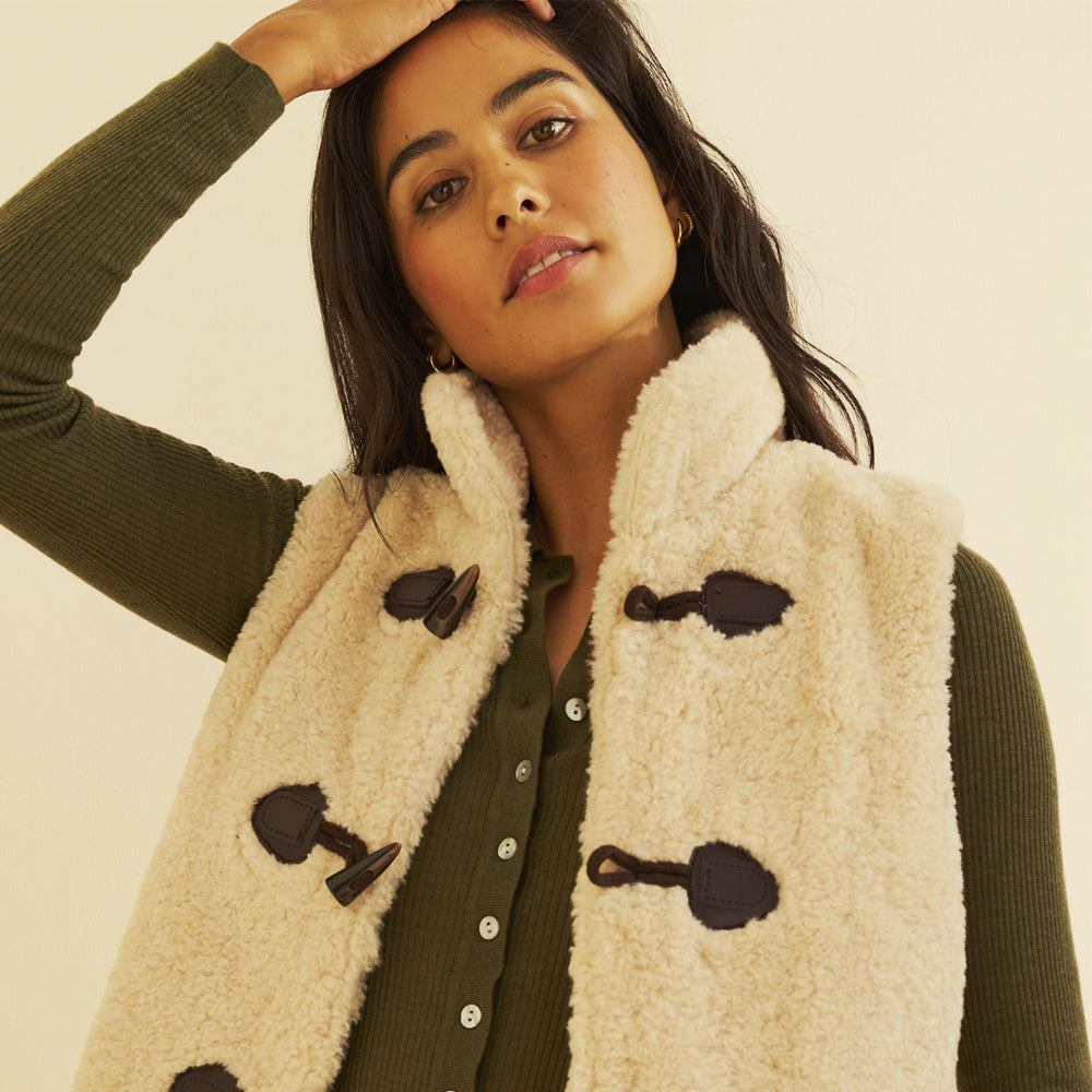 Close-up of a women’s cream sherpa vest showing dark brown duffle toggles and a plush stand collar.