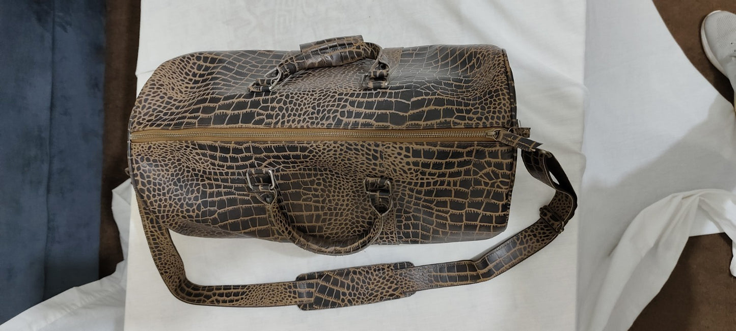 Close-up top view of the croc-texture leather duffle showing robust brass zippers and carry handles