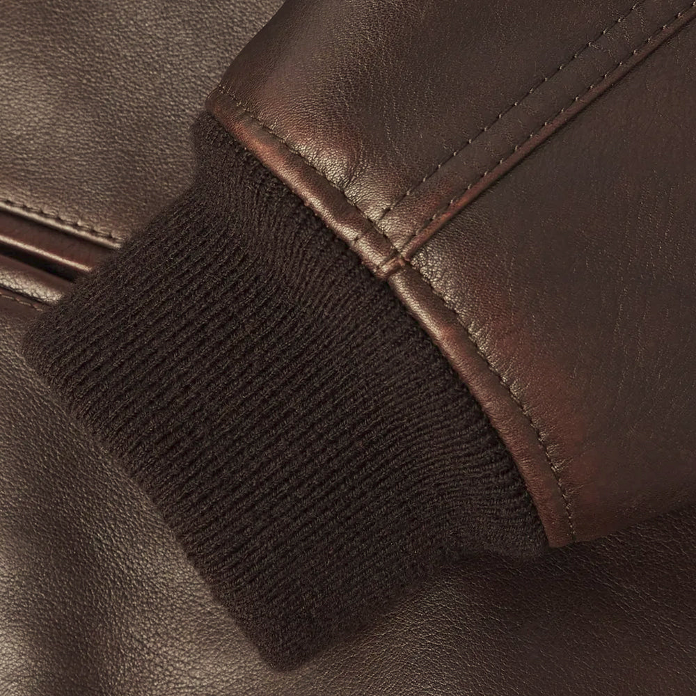 Macro view of the dark rib-knit cuff joined to a tonal-stitched waxed lambskin bomber sleeve
