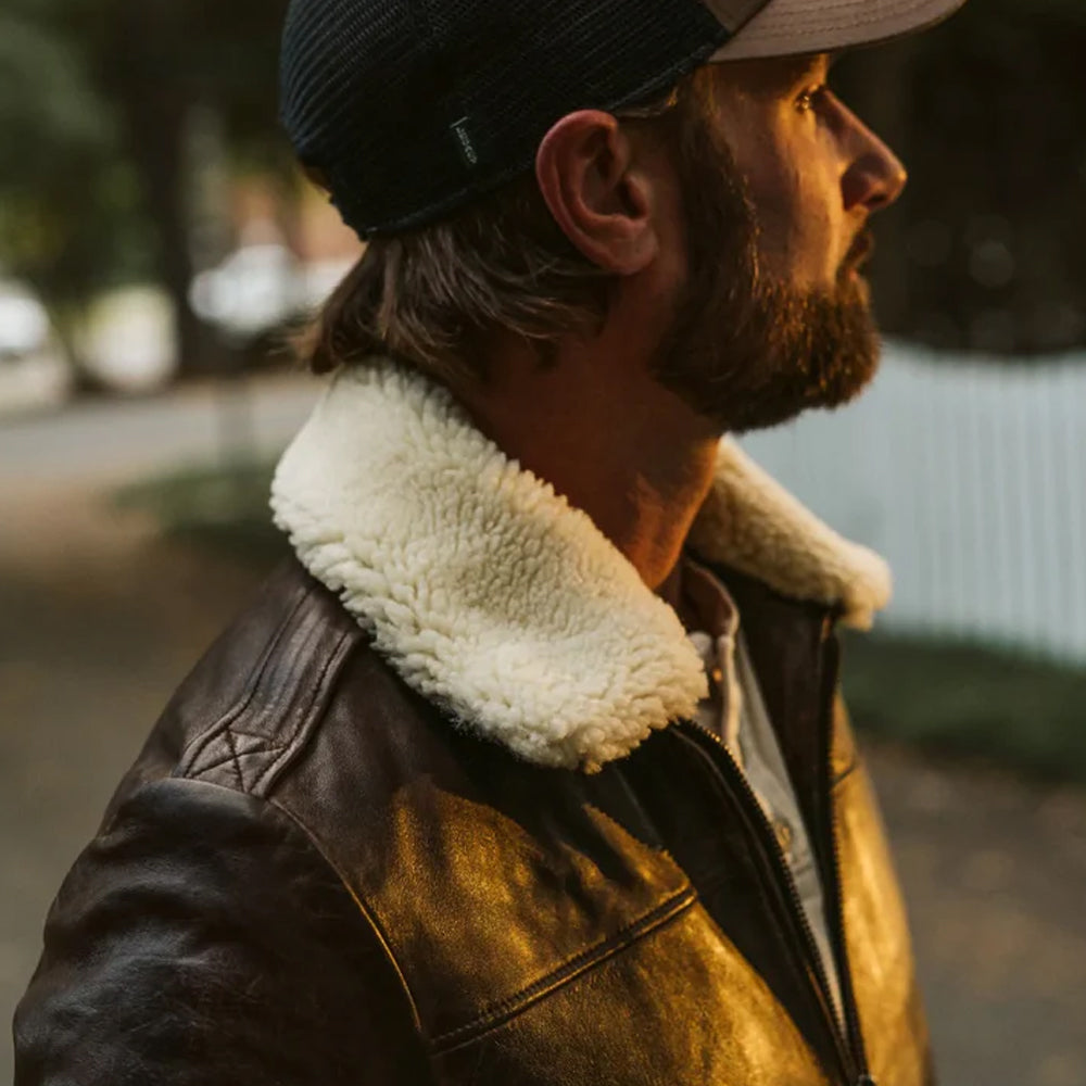 Side profile close-up of a man showcasing the thick texture of the removable cream shearling collar on a vintage brown leather jacket.