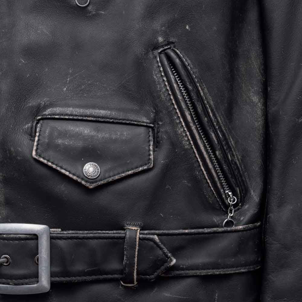 Close-up of snap coin pocket, angled zip hand pocket and silver buckle on distressed black leather biker jacket