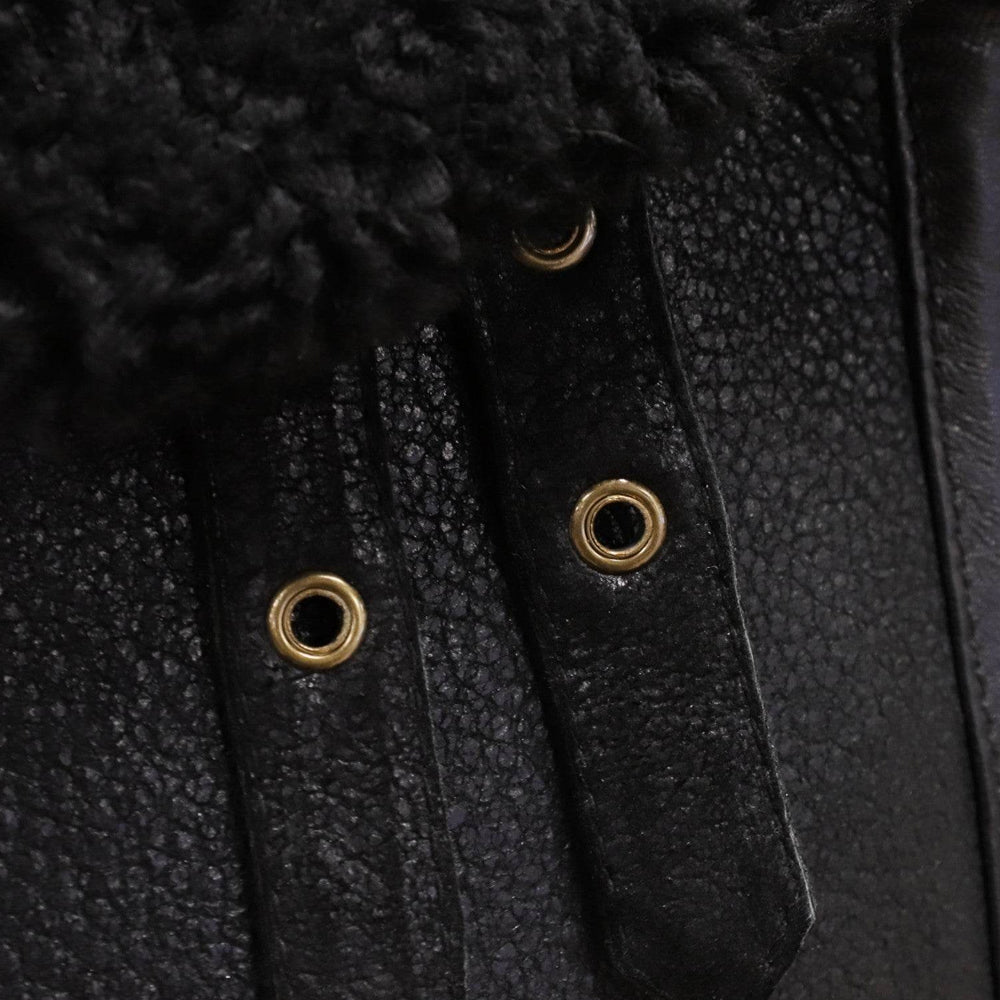 Close-up of perforated black leather throat straps with antique-brass eyelets on a shearling flight collar